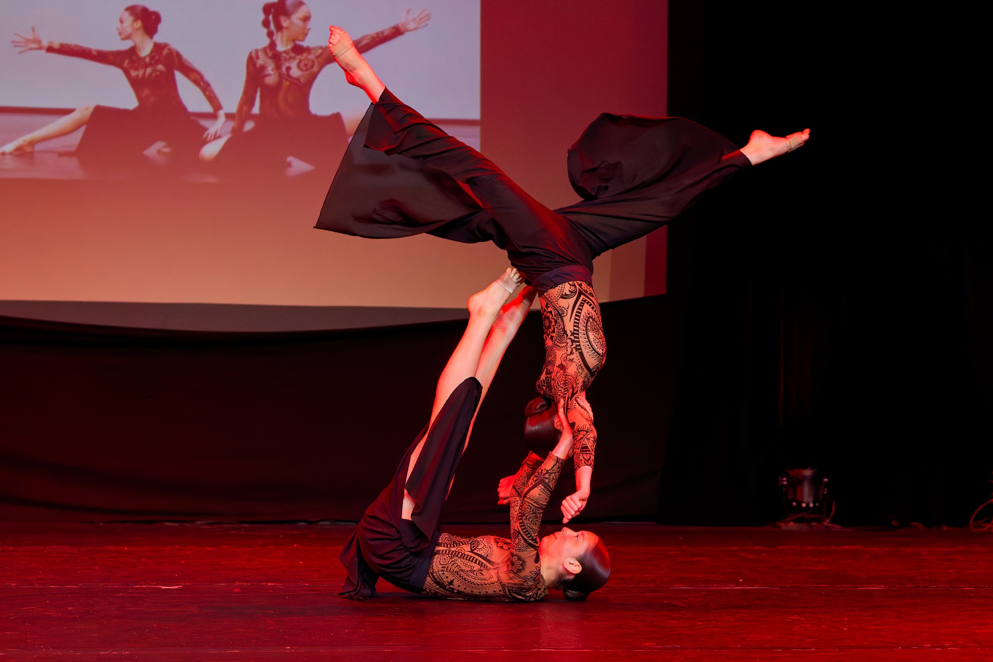 Deux danseuses réalisent une figure acrobatique au sol sous une lumière rouge