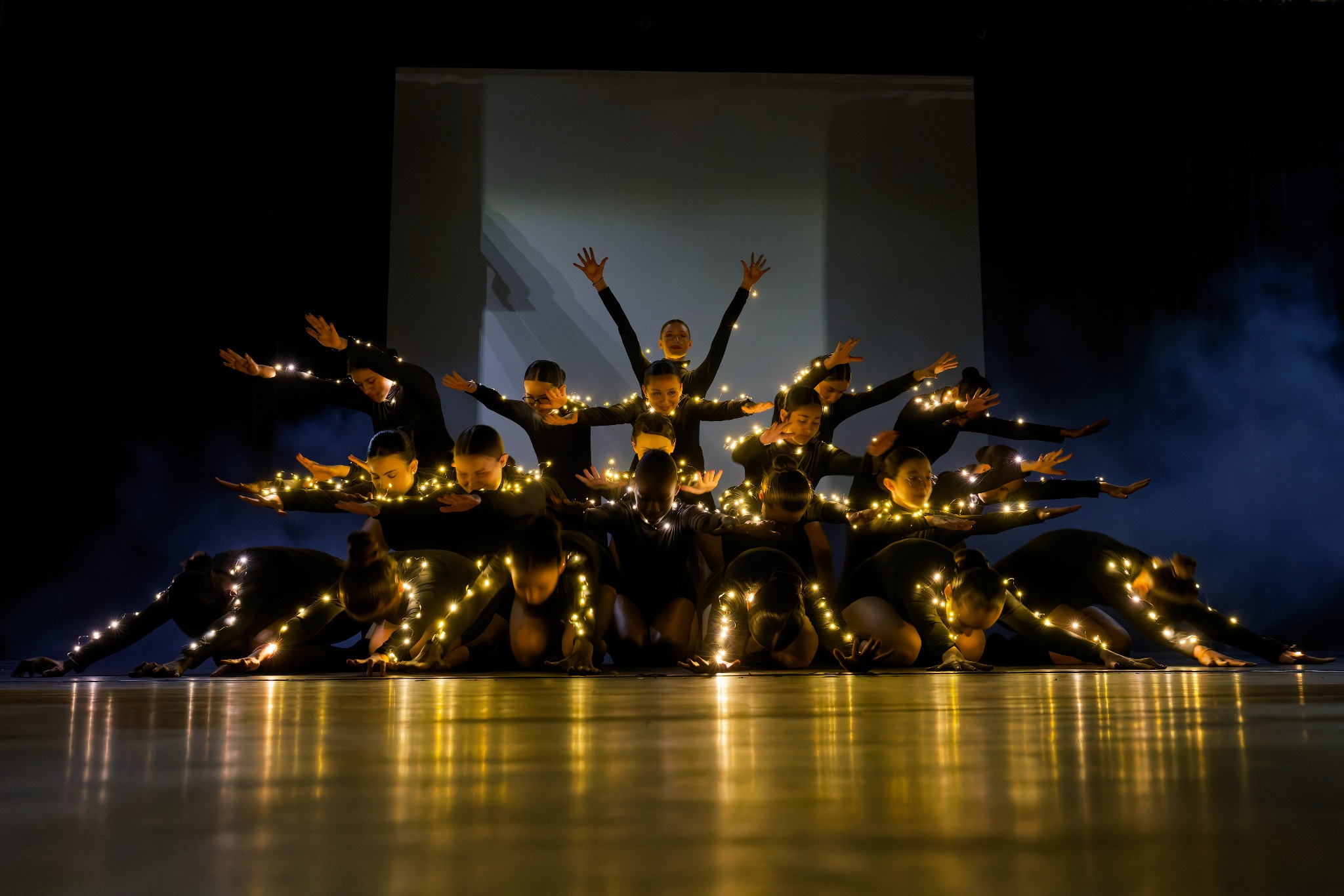 Un groupe de danseuses portant des guirlandes lumineuses compose une figure sur scène