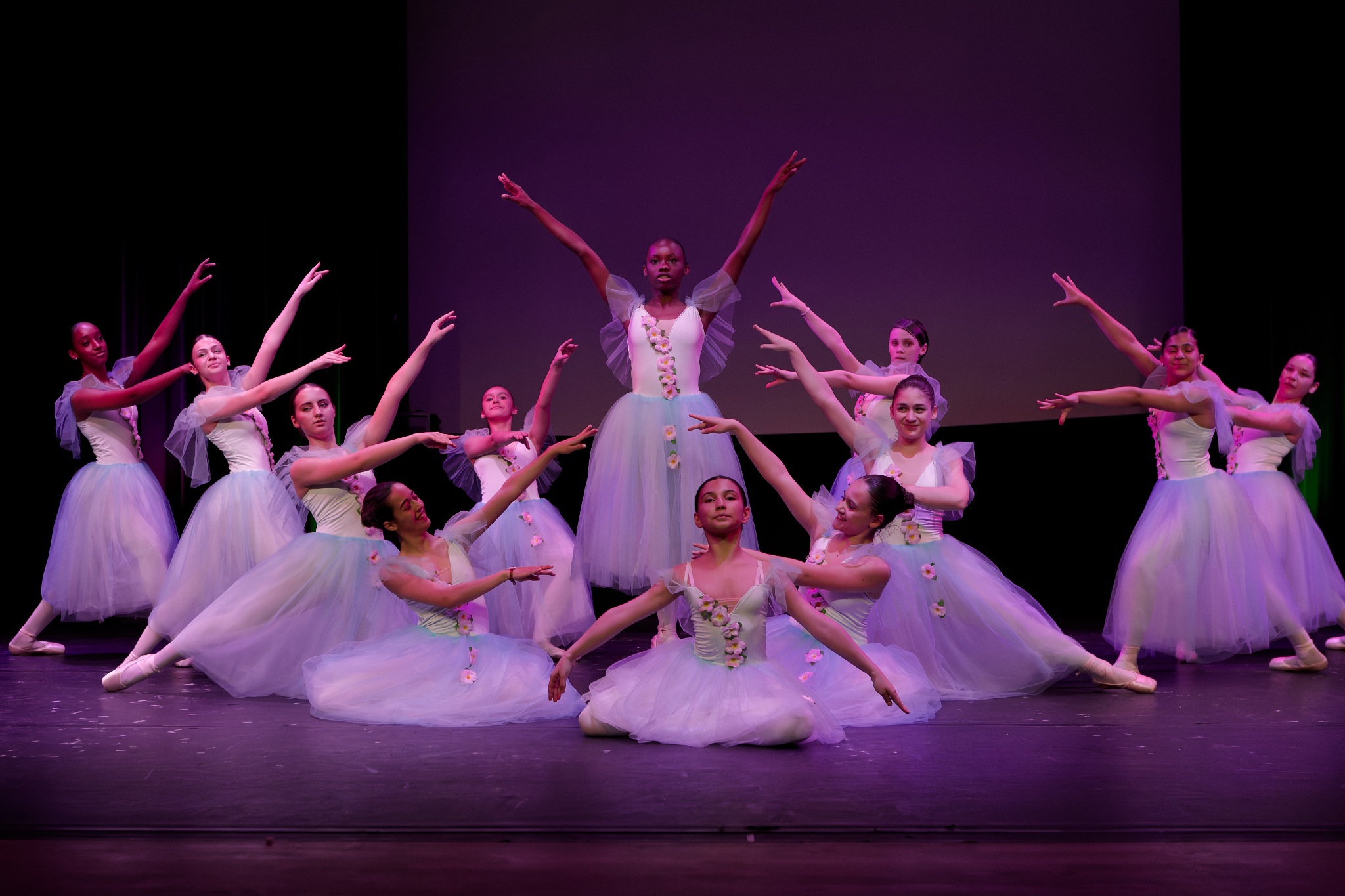 Un ensemble de danseuses en robes claires forme un tableau sur scène, les bras levés